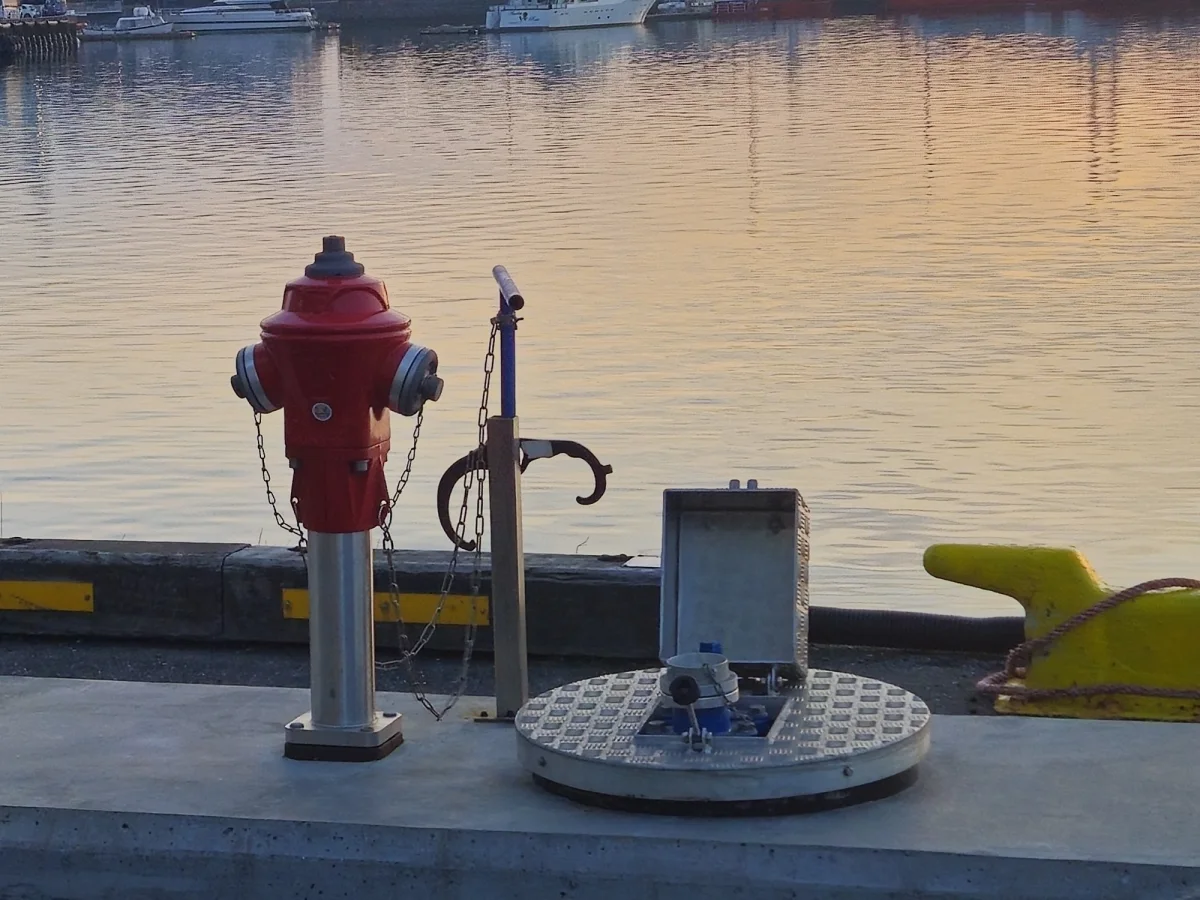 Water fittings on the quay in Reykjavik at sunset: the red hydrant, the standpipe with its hose coupling and the round flush service point set into the concrete.