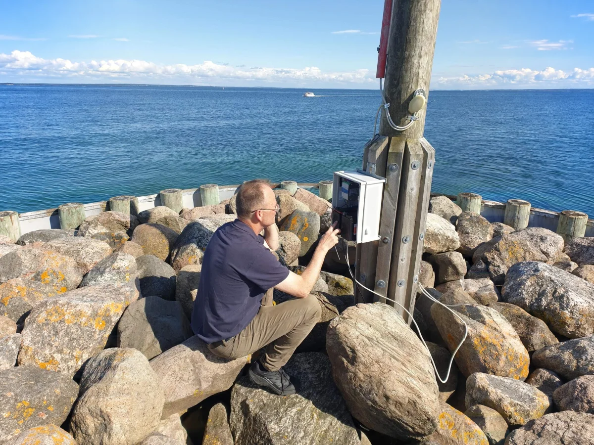 Technician working on the OceanWatcher controller at a timber post on the rocks, with open sea behind.