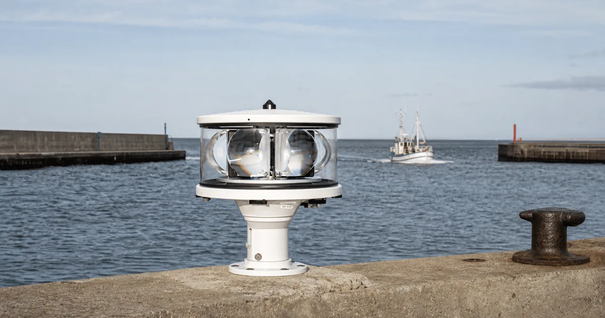 A Beacons pier light marks the centre of a wide Danish harbor entrance scene with a fishing vessel beyond.