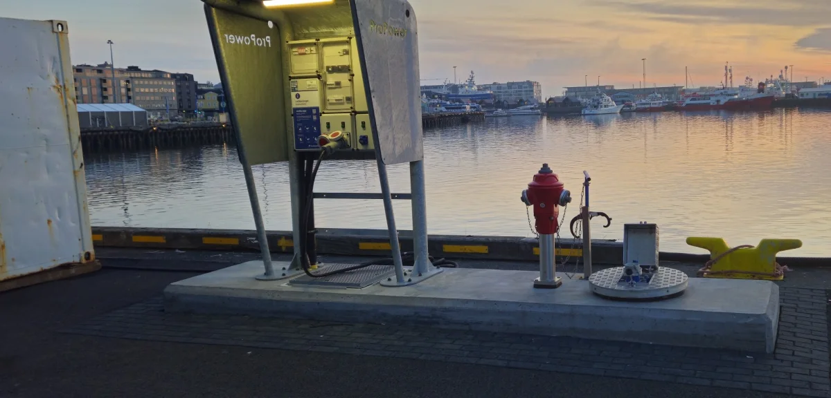 Wide view along the quay at sunset, with the supply pedestal, the hydrant, the standpipe, the service point and the mooring bollard in one line.