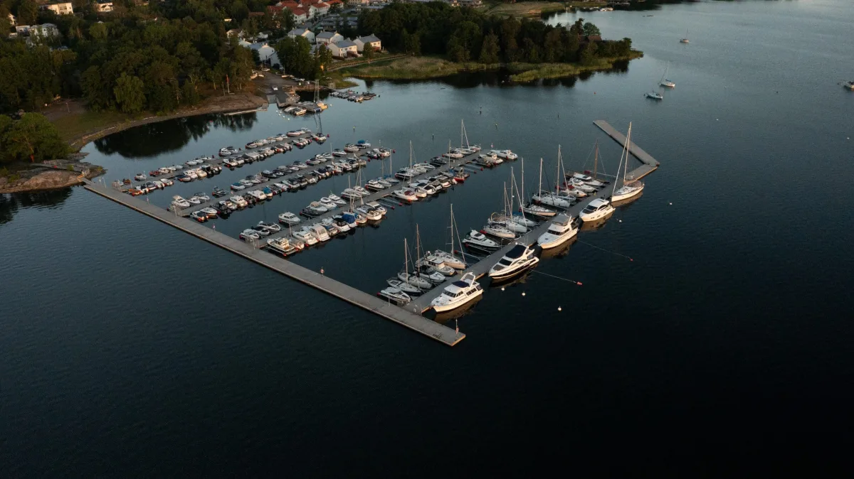 Aerial view of a marina with floating piers, boats and a surrounding concrete pontoon.