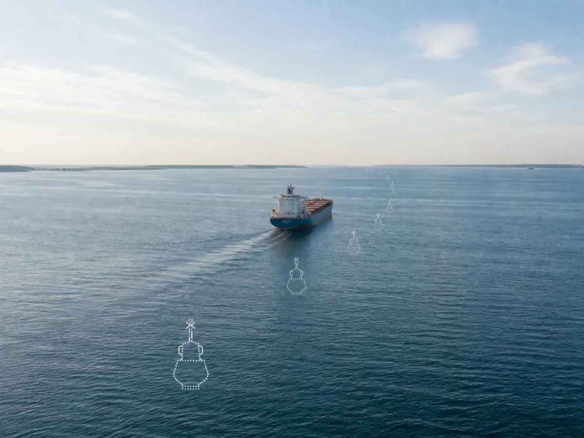A cargo ship follows a fairway marked by a curved line of glowing dotted virtual buoy outlines on the open sea.
