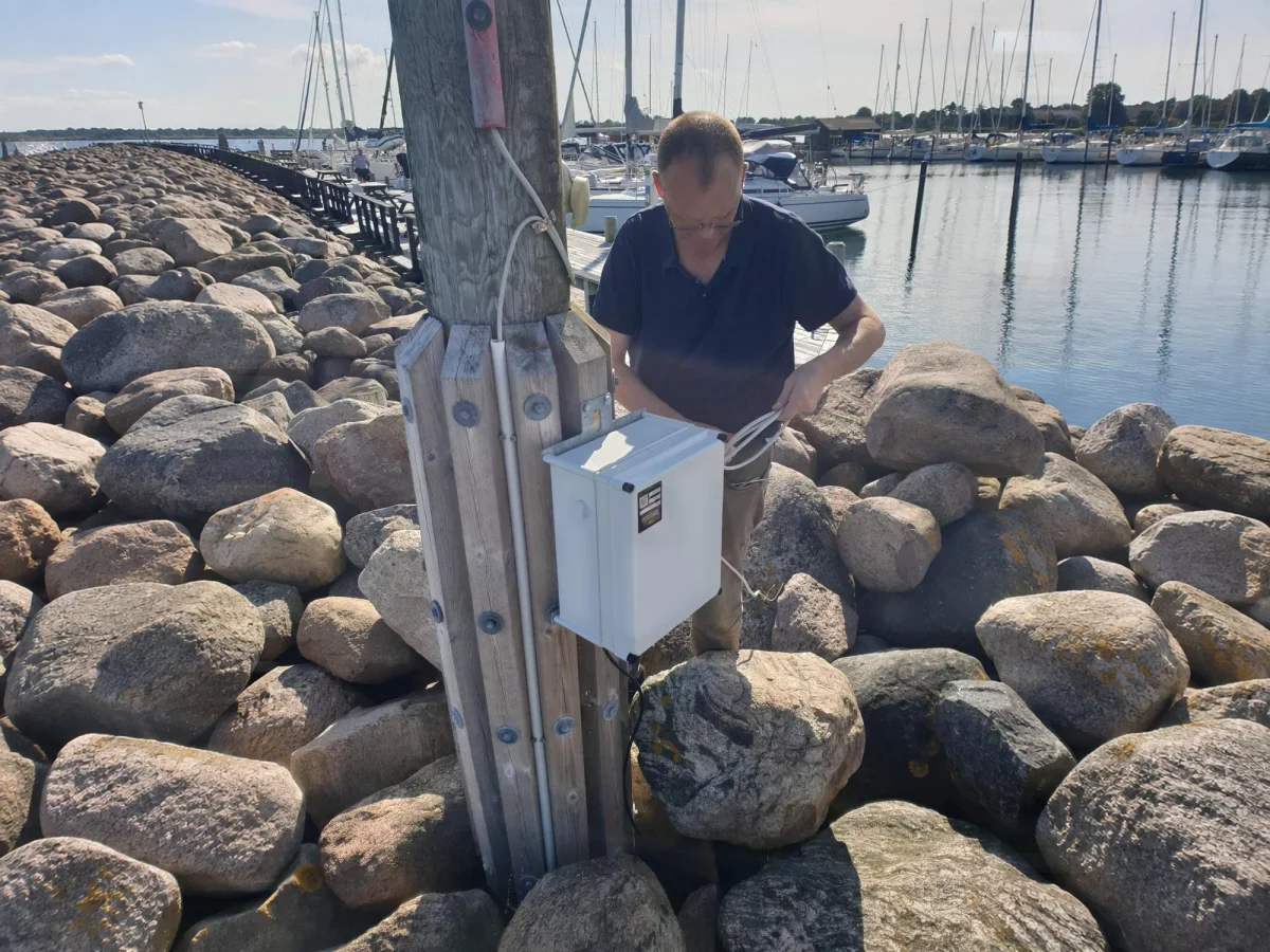 Technician opening the OceanWatcher controller box on a timber post, with the marina behind.