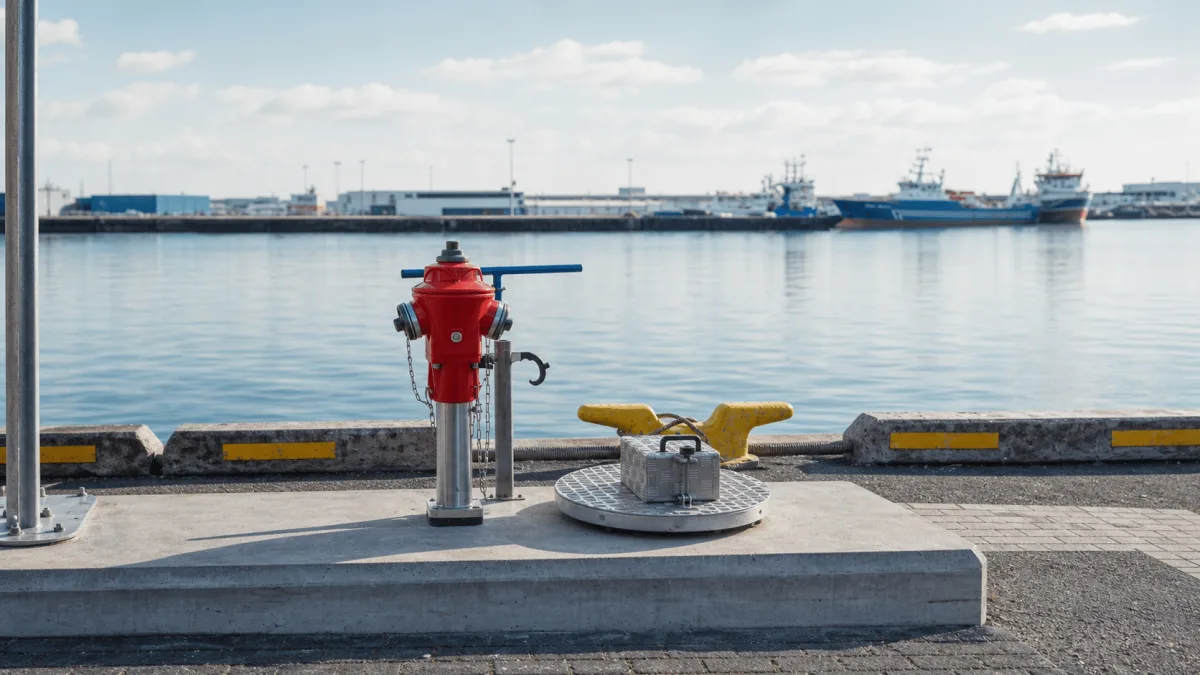 WaterStation well installation with a red riser, blue valve handle and stainless control box on a calm Nordic harbor pier.