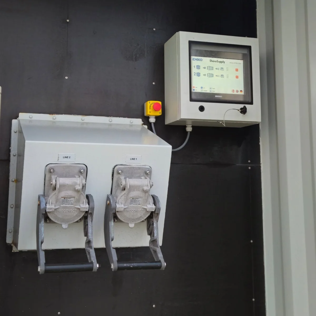The ShoreSupply control panel on the container wall: the EMIKO touch screen, the emergency stop and the two heavy connectors marked LINE 1 and LINE 2.