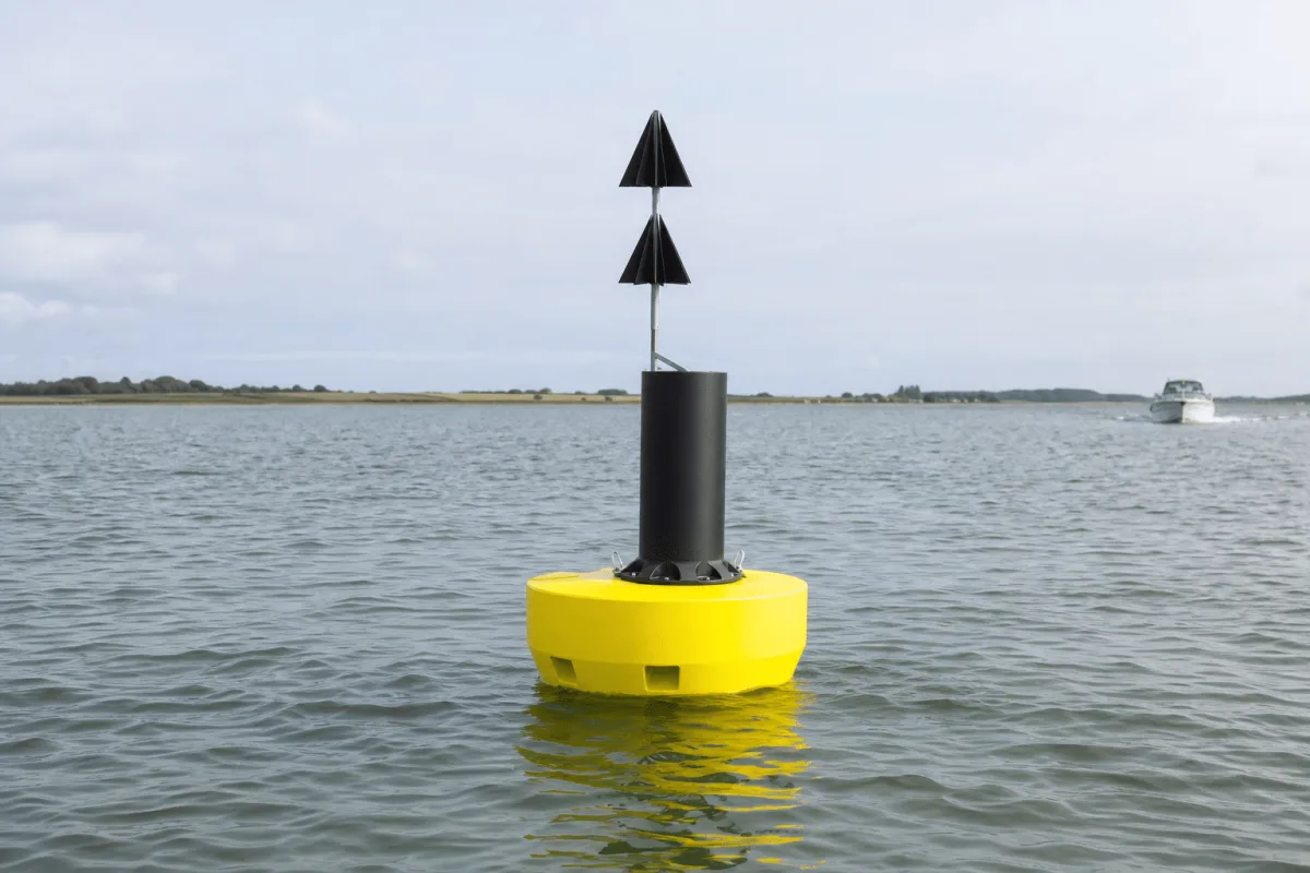 Physical Buoys FLC navigation buoy floating in calm Danish coastal water with a small work boat in the distance.