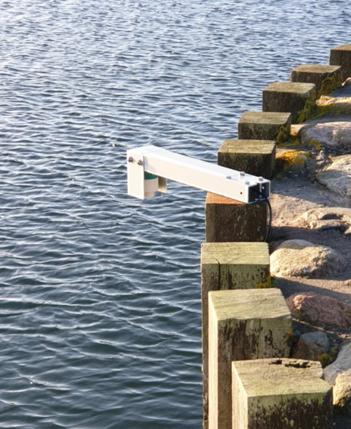 The OceanWatcher arm seen from above, reaching over the water from the timber wall of the breakwater.