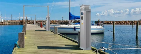 Utility pedestals along a wooden marina pier beside sailing boats.