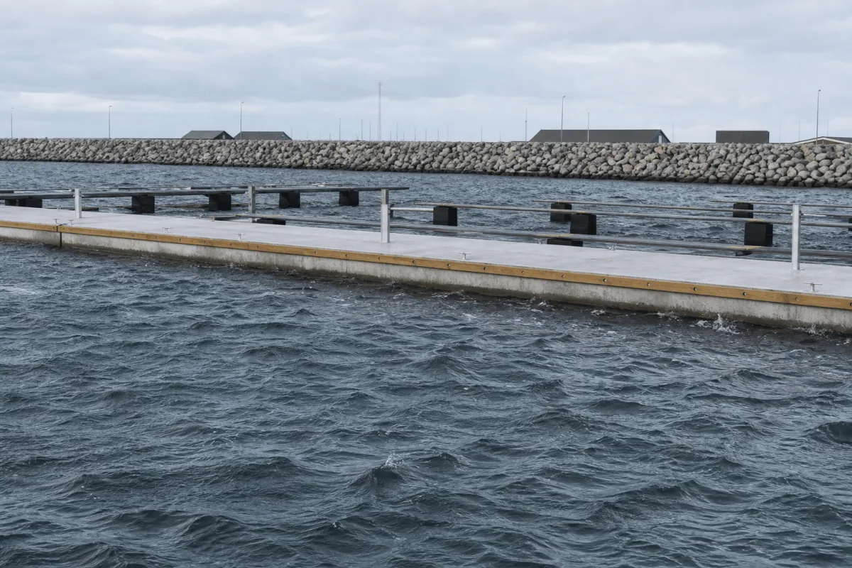 Vikingegaarden concrete pontoons remain level in choppy marina water with a stone breakwater behind.