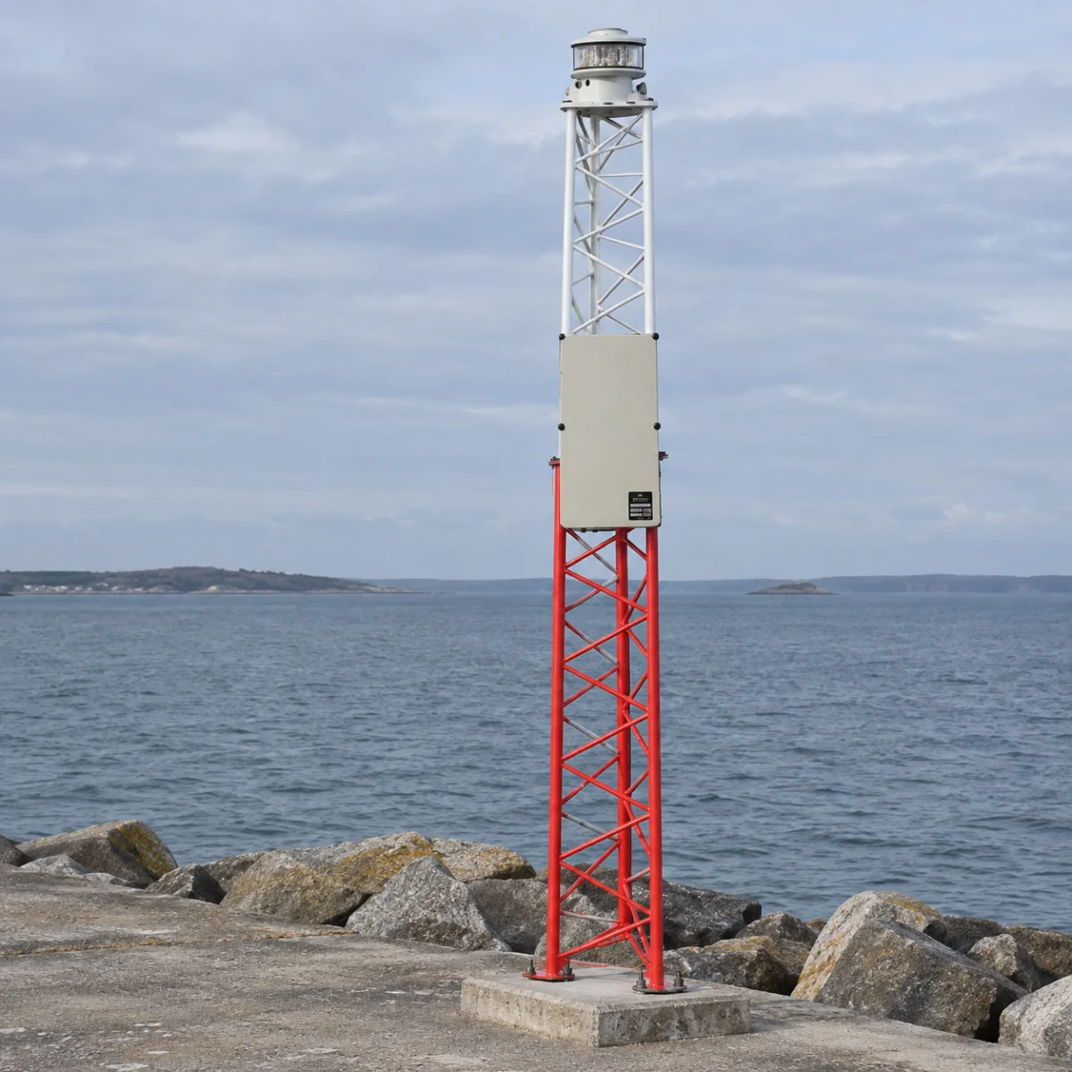 The equipment cabinet mounted inside the lattice of a MarineGuard beacon on a breakwater, with the lantern directly above it.