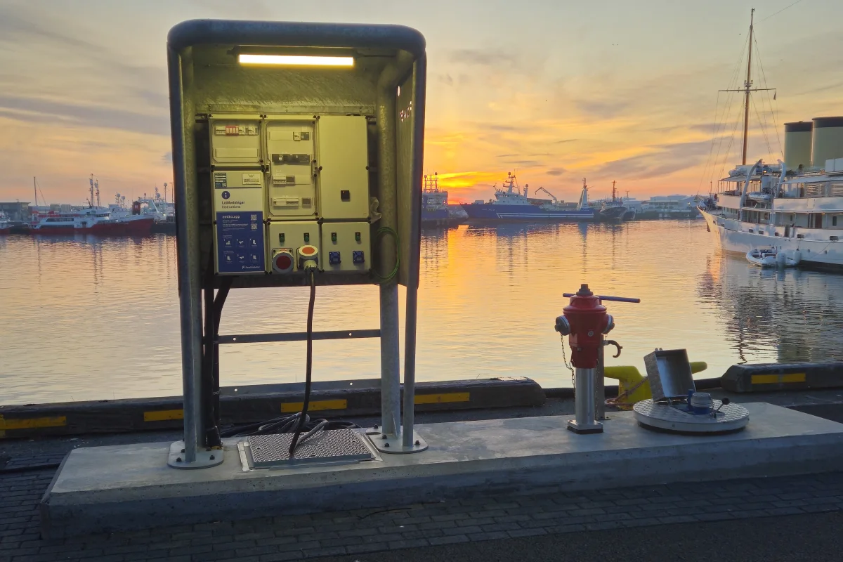 Vandgruppen på kajen i Reykjavik ved solnedgang: standeren oplyst under skærmen, den røde brandhane og det nedfældede servicepunkt, med havnen bagved.