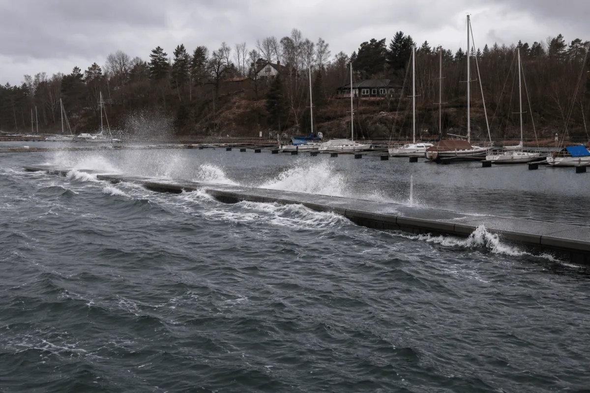 Winter waves spray across the outer side of a Vikingegaarden floating breakwater while the moorings behind remain calm.