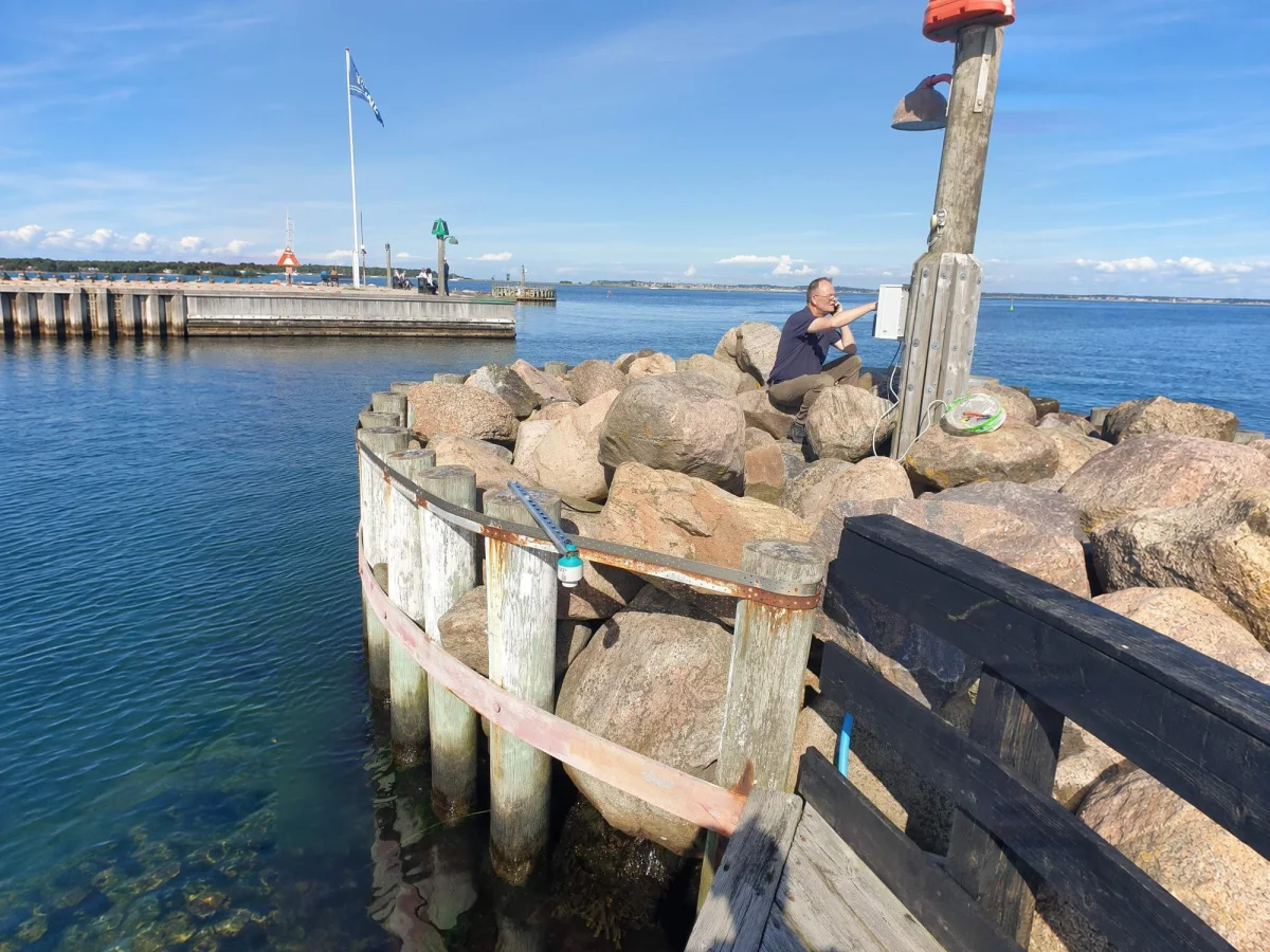 OceanWatcher installation on a timber breakwater, with the mounting arm and the rocks of the shore.
