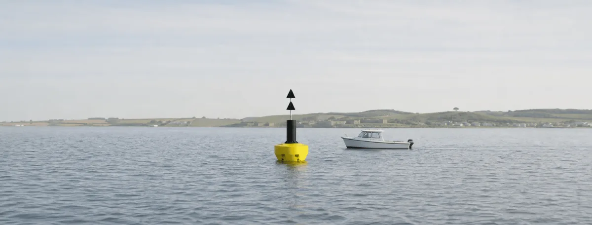 Physical Buoys FLC navigation buoy and a small work boat crossing a wide Danish harbor approach.