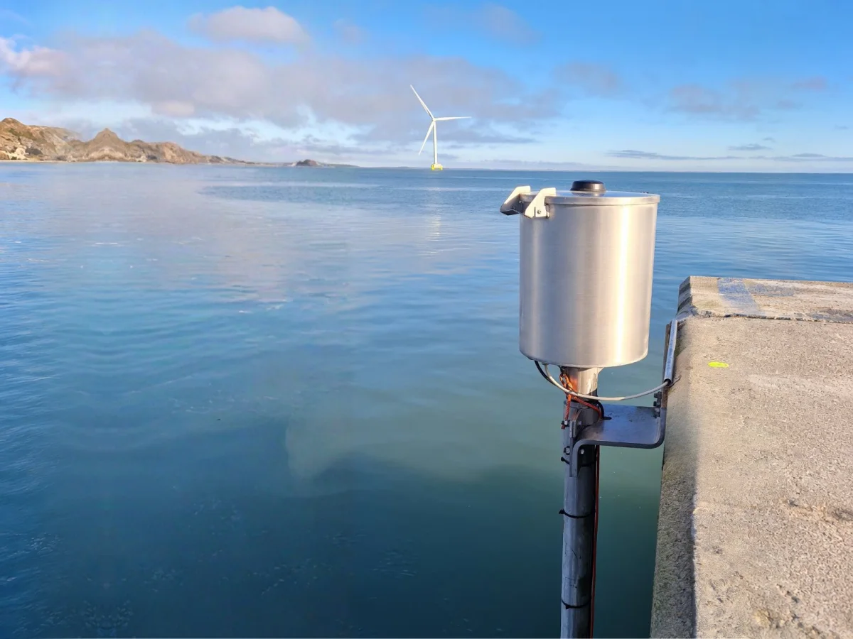 OceanWatcher WCM 100 current monitor: a stainless steel canister on a vertical pole at the edge of a pier.