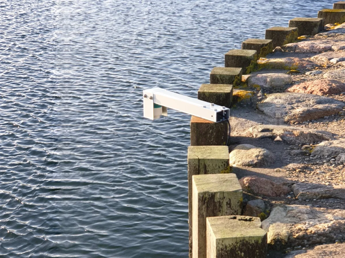 White aluminium arm cantilevered out over calm water, holding the OceanWatcher radar sensor above the surface.
