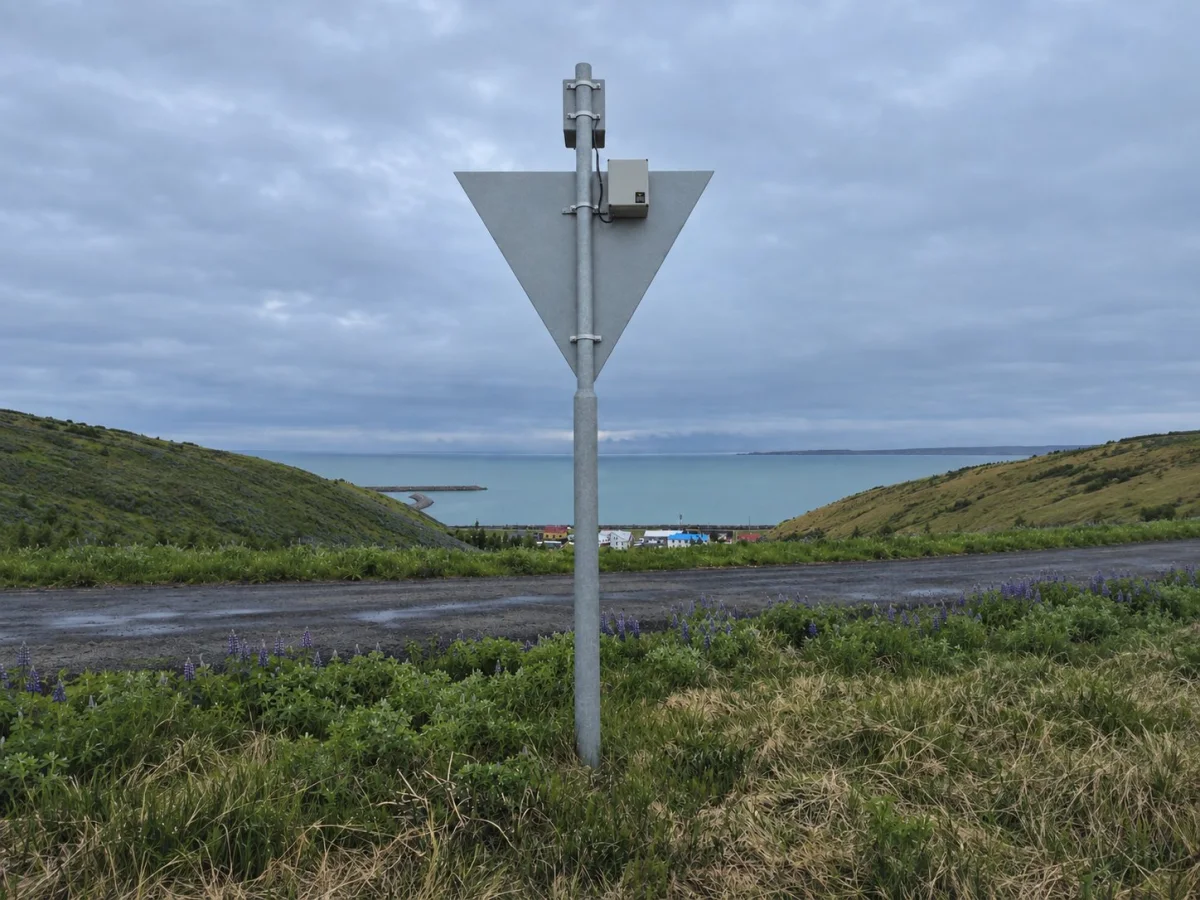 PowerGuard enclosure on the post of a grey daymark above a coastal road, with the town and the bay beyond.