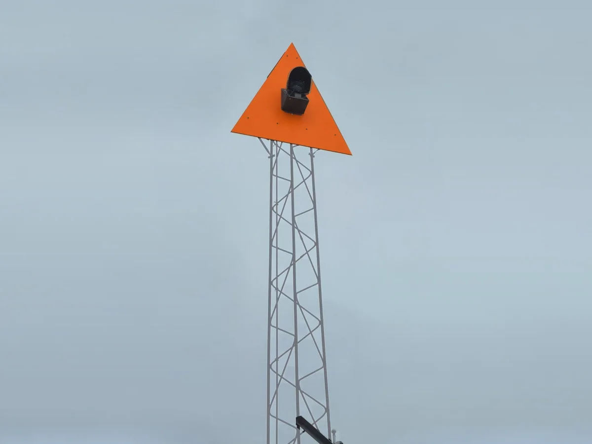 Lattice mast carrying an orange triangular daymark and a light, powered without a mains connection.