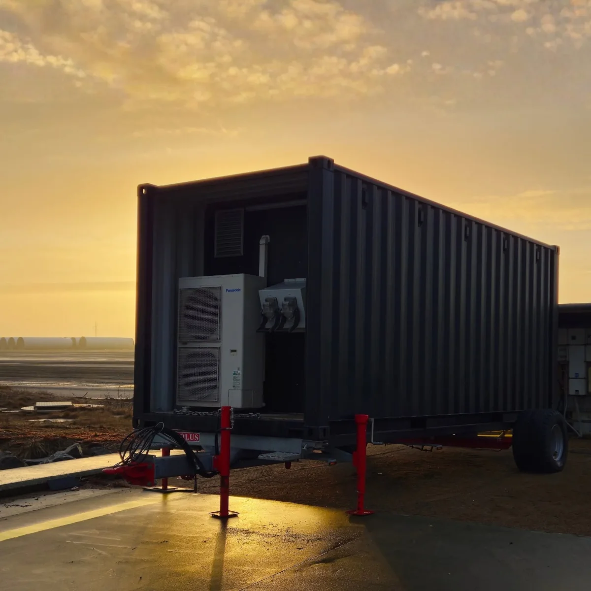 ShoreSupply container on its road trailer at sunrise, standing on its red support legs with the equipment bay open on the cooling unit and the cable connectors.
