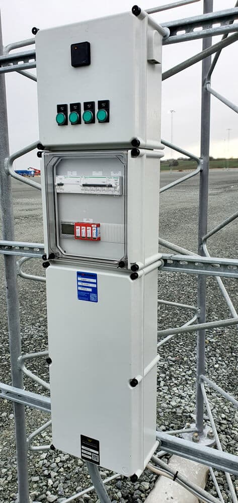 Outdoor lighting-control cabinets mounted on a lattice structure, with green push buttons and a clear electrical panel.
