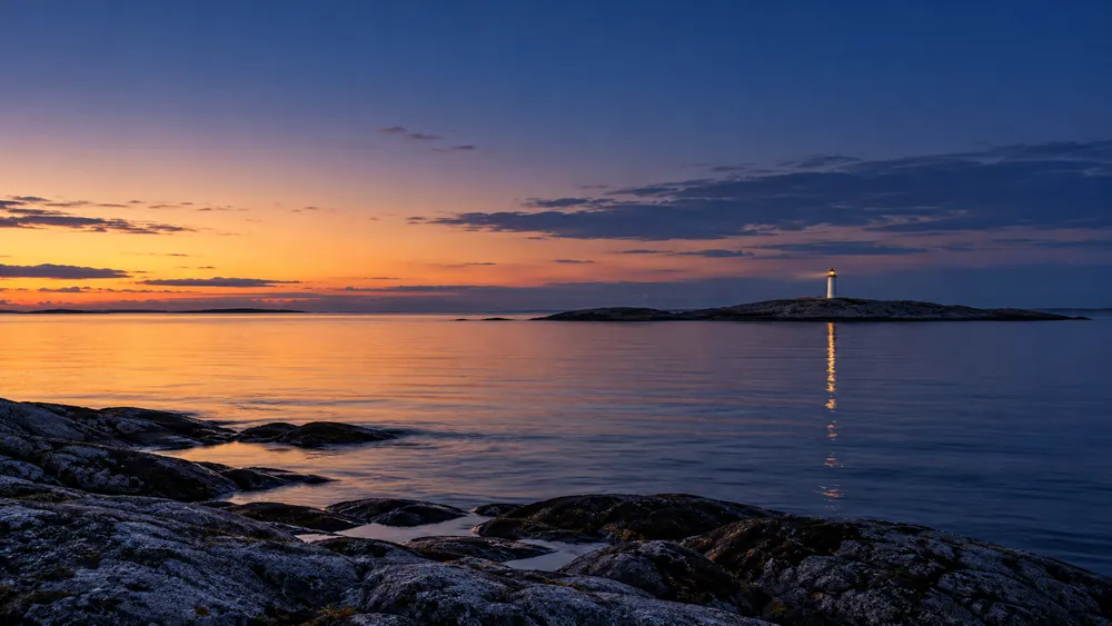 Et fjernt fyr på en lav klippeø i tusmørke, med lanternen tændt