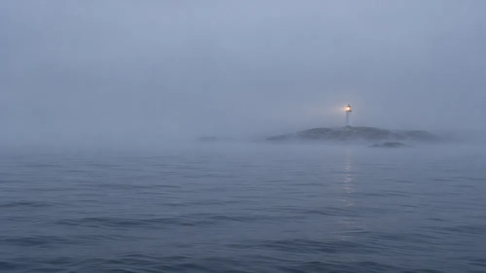 Et fyr, der svagt anes langt væk i morgentåge over havet