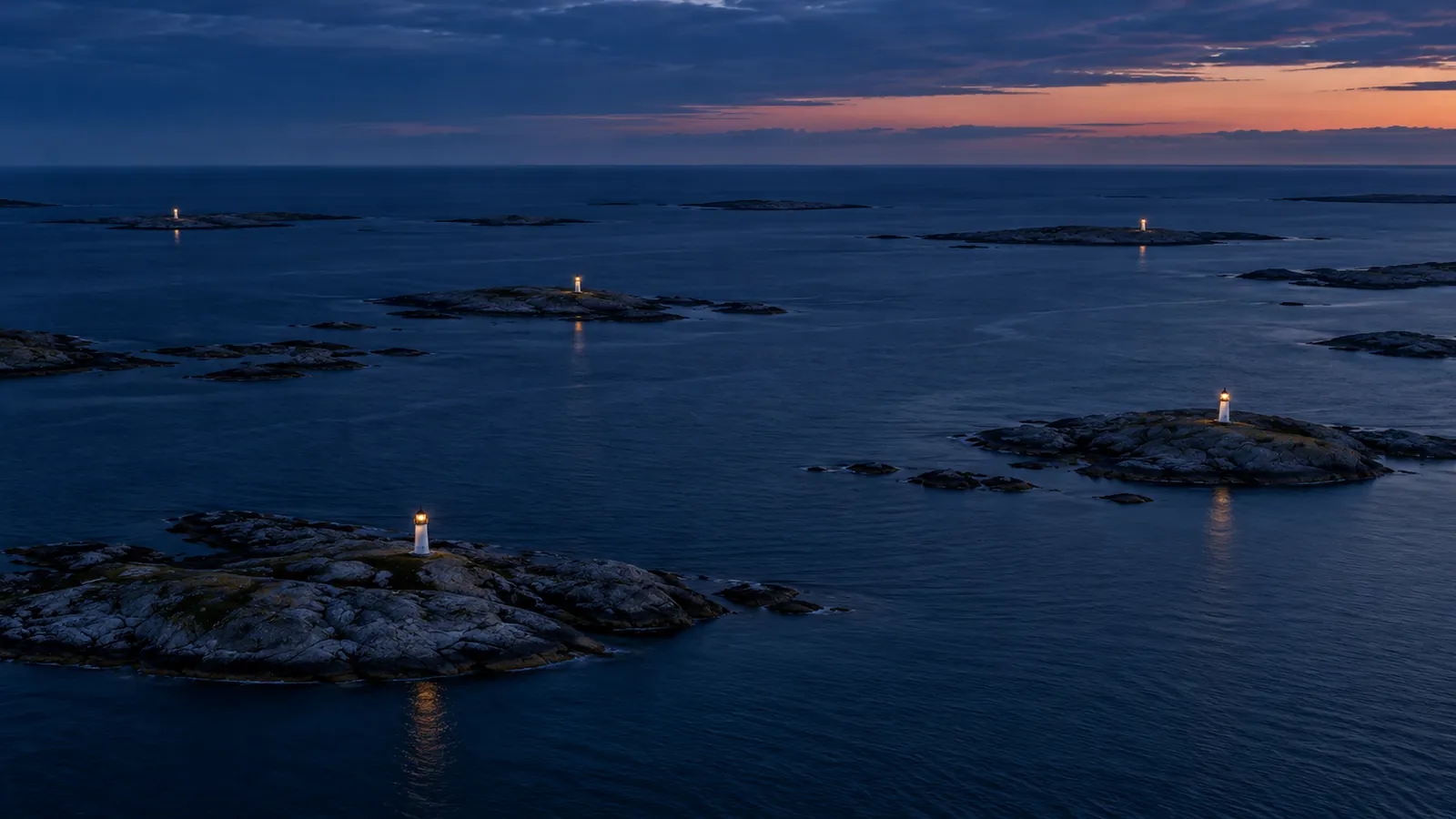 Luftfoto i skumringen af en skærgård med små fyr på hver sit skær